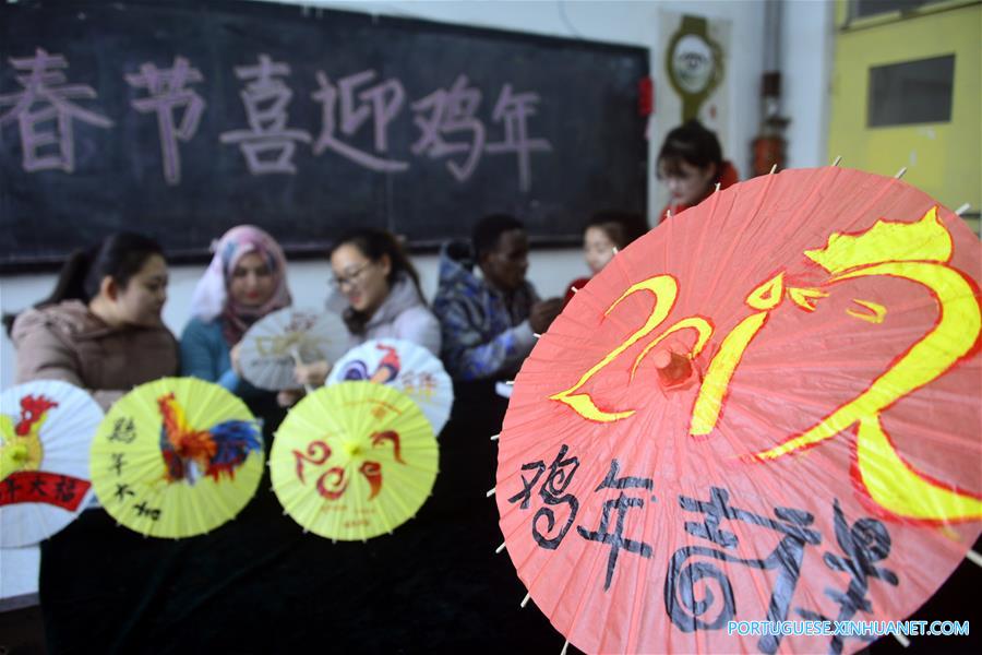 Estudantes internacionais pintam temas de galo em sombrinhas de papel chinesas