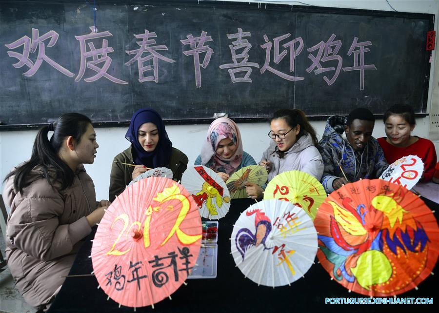 Estudantes internacionais pintam temas de galo em sombrinhas de papel chinesas
